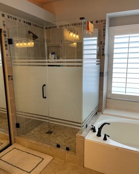 Bathroom with glass shower enclosure and bathtub added decor with window film on glass doors